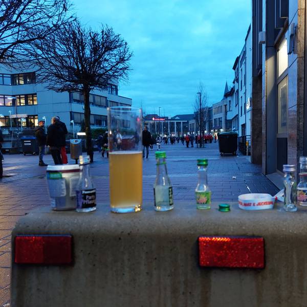 Leere Schnapsfläschchen und ein halbleeres Bierglas, bunte Flaschendeckel auf einer Betonsperre.