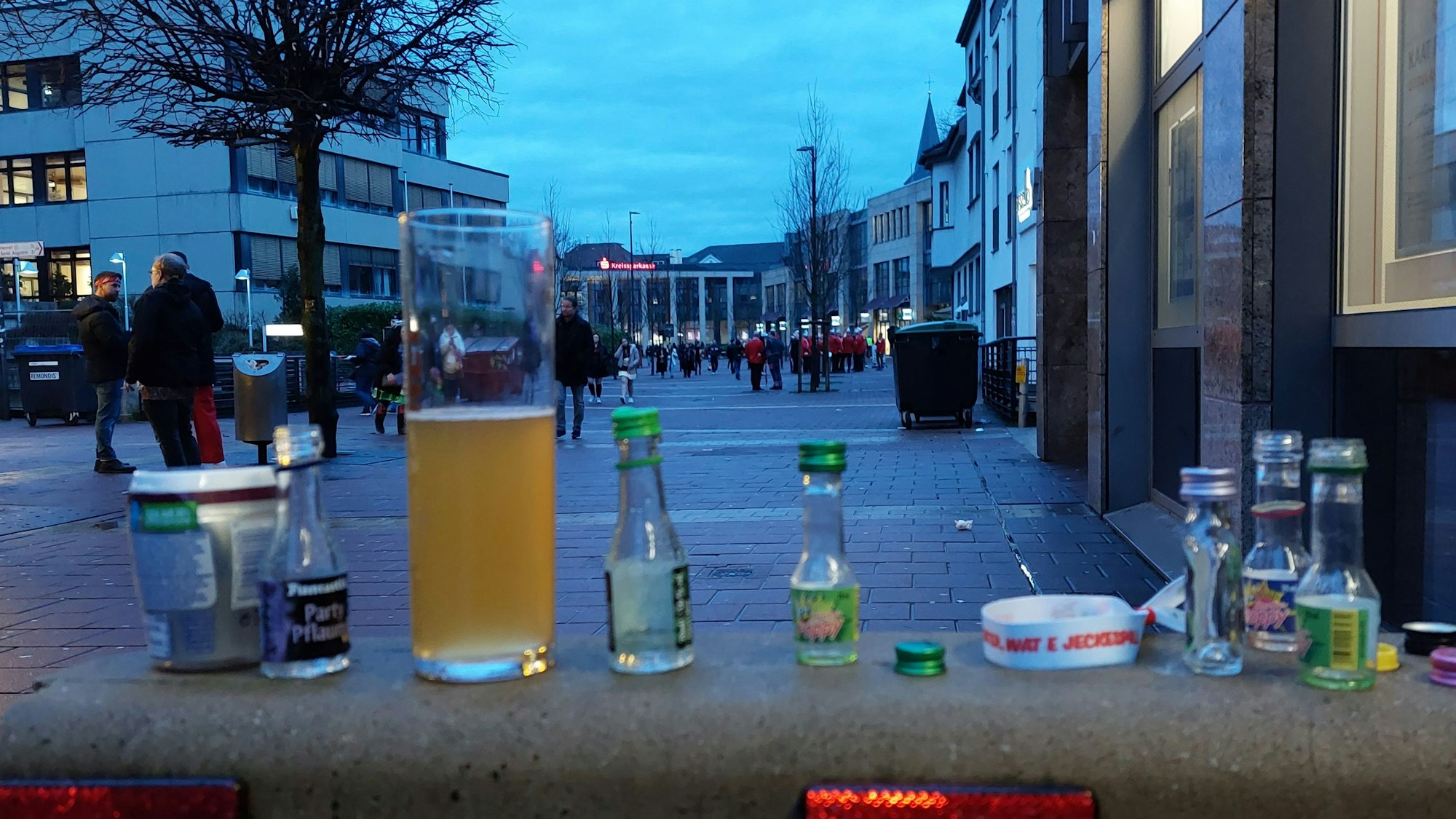 Ein halbvolles Bierglas und kleine Schnapsfläschchen auf einem Betonsockel.