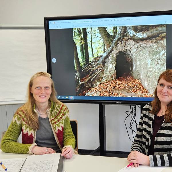 Katrin Oberländer (l.) und Bibliotheksleiterin Michelle Wagner sitzen an einem Tisch. Im Hintergrund ist ein Foto vom Römerkanal zu sehen.