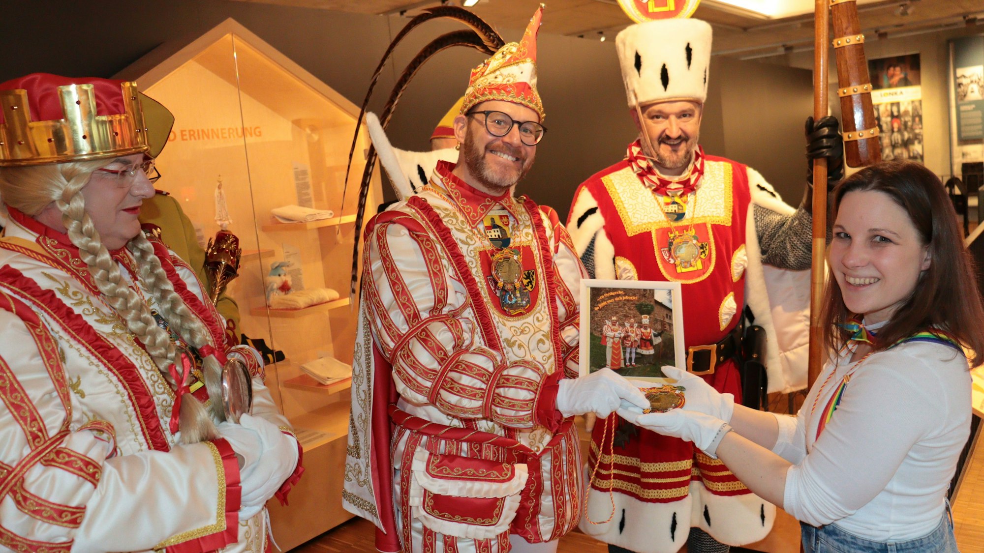 Prinz Tobi I., der von Jungfrau Martina und Bauer Sascha flankiert wird, überreicht den Orden und ein Foto an Museumsmitarbeiterin Maja Kützemeier.