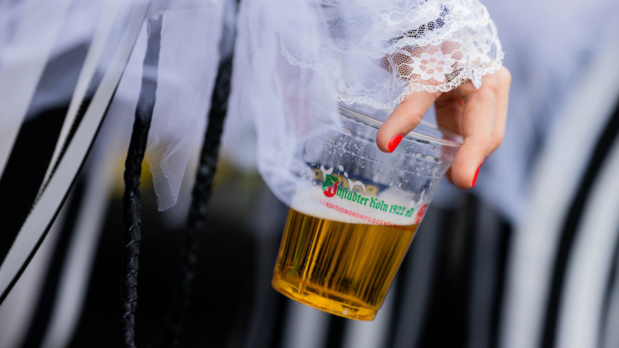Eine verkleidete Person hält einen Plastikbecher in der Hand, der zur Hälfte mit Bier gefüllt ist