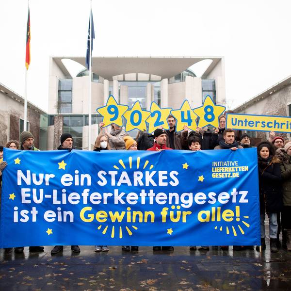 Vor dem Bundeskanzleramt in Berlin hält eine kleine Gruppe von Demonstranten ein blaues Transparent mit der Aufschrift „Nur ein starkes EU-Lieferkettengesetz ist ein Gewinn für alle!“