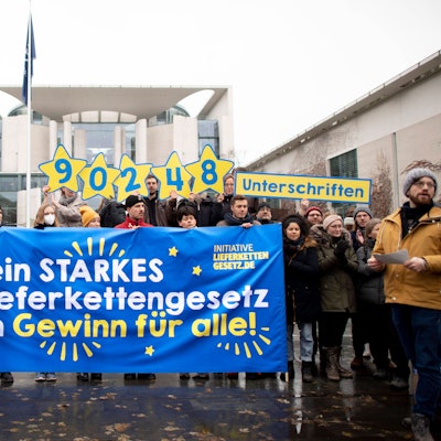 Vor dem Bundeskanzleramt in Berlin hält eine kleine Gruppe von Demonstranten ein blaues Transparent mit der Aufschrift „Nur ein starkes EU-Lieferkettengesetz ist ein Gewinn für alle!“