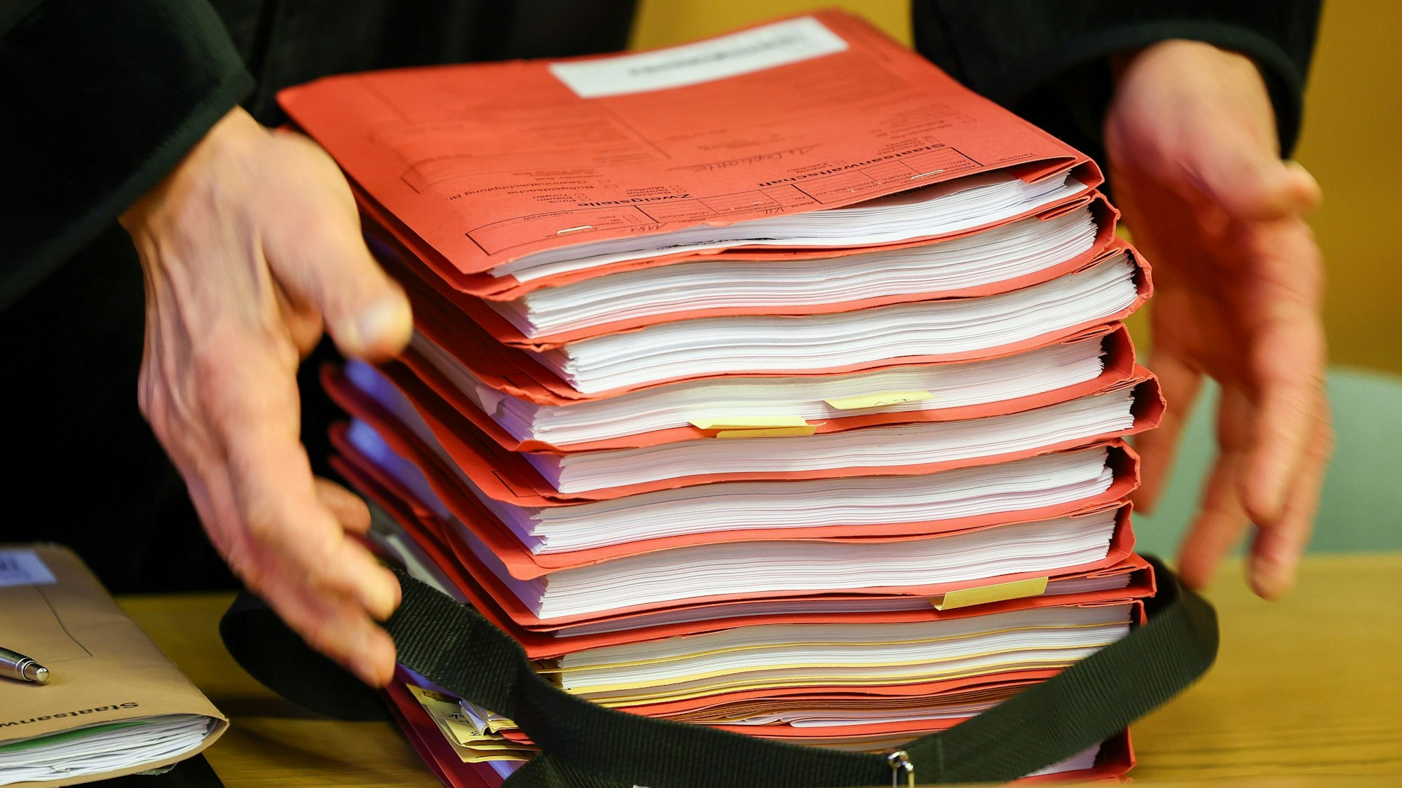 Der Staatsanwalt legt einen Stapel Akten zu Prozessbeginn auf einen Tisch in einem Saal im Landgericht.