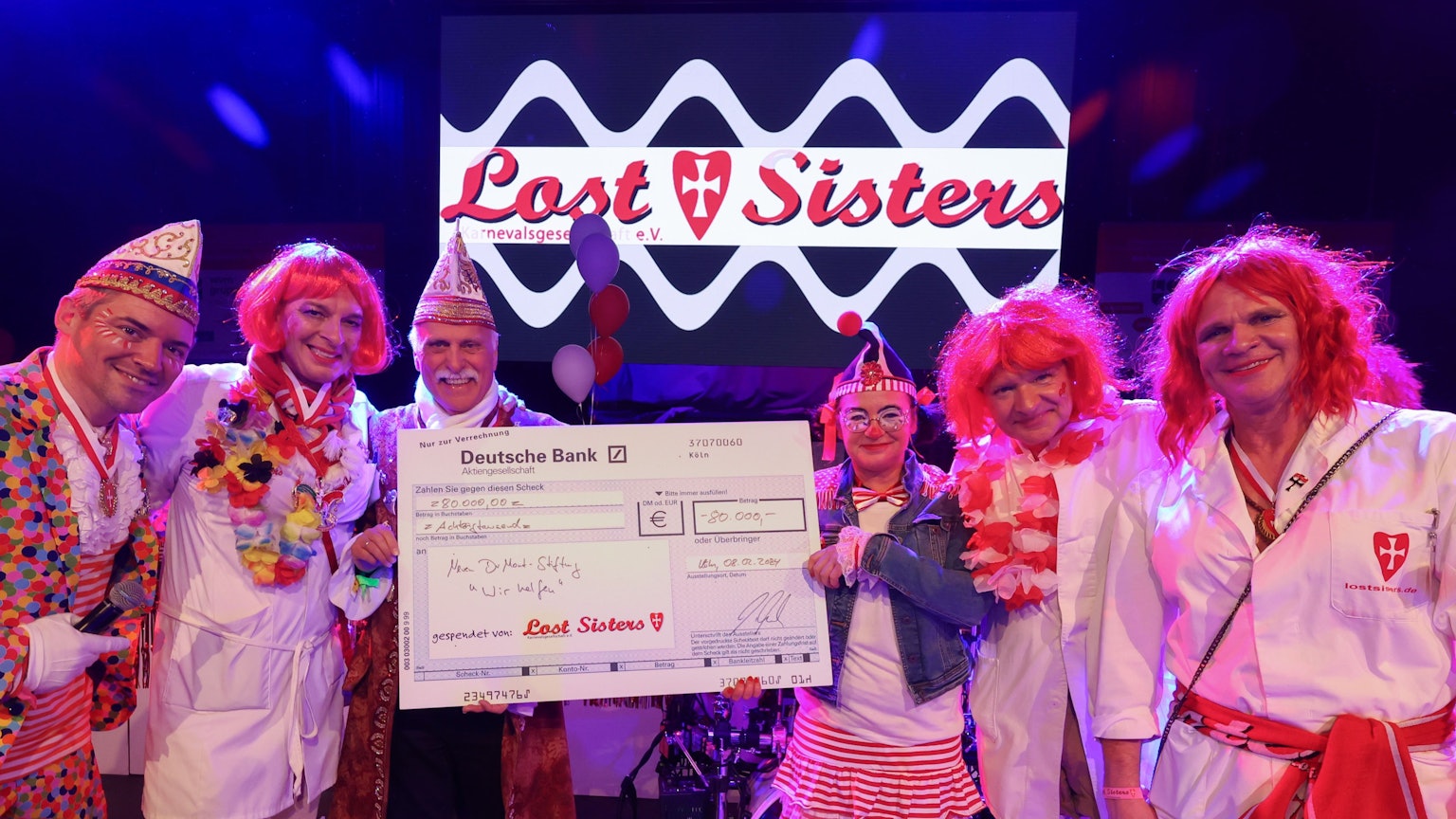 Die Lost Sisters überreichen Karl-Heinz Goßmann (Geschäftsführer „wir helfen“) und „wir helfen“-Redakteurin Caroline Kron einen symbolischen Scheck über 80.000 Euro.