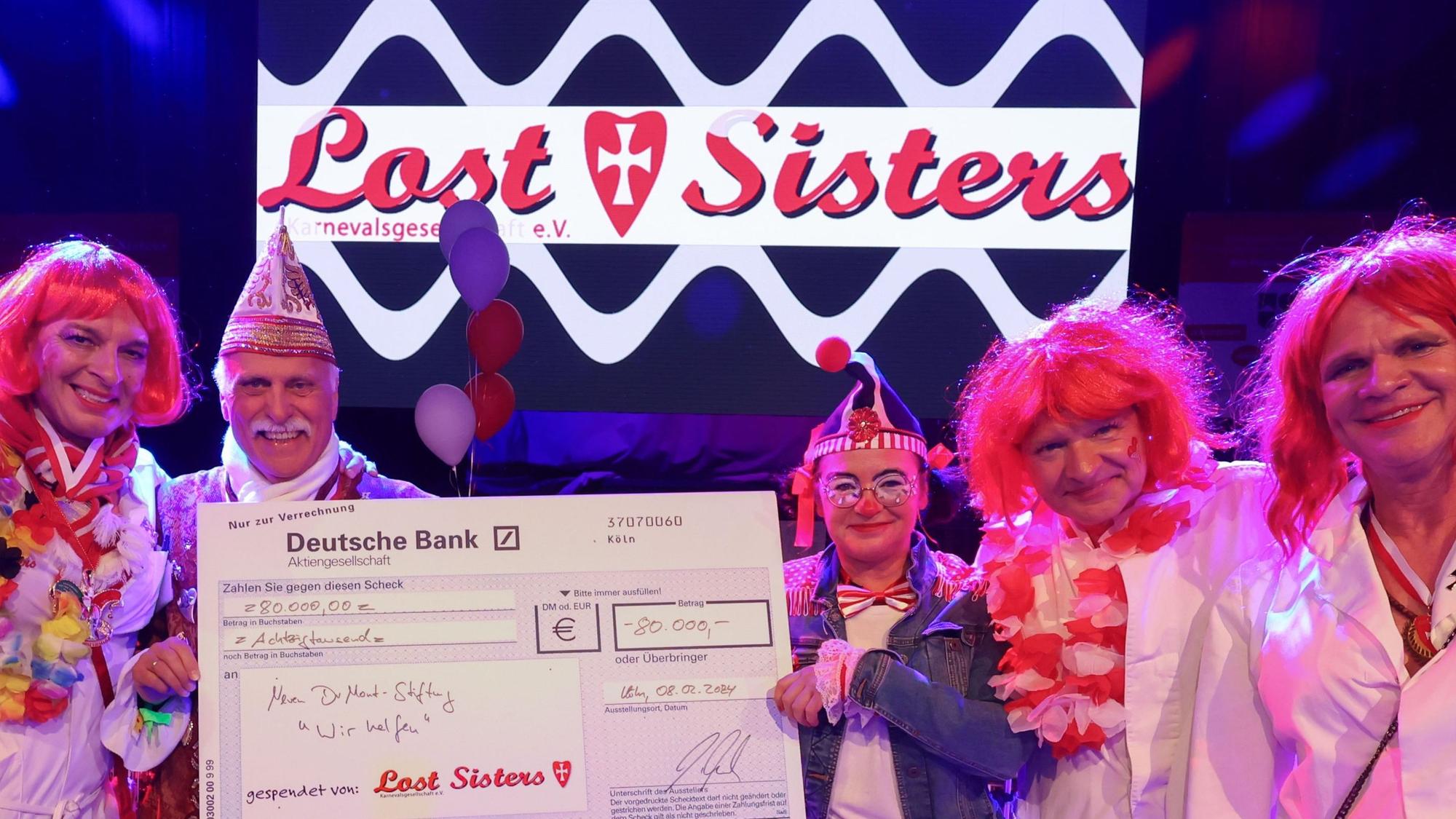 Die Lost Sisters überreichen Karl-Heinz Goßmann (Geschäftsführer „wir helfen“) und „wir helfen“-Redakteurin Caroline Kron einen symbolischen Scheck über 80.000 Euro.