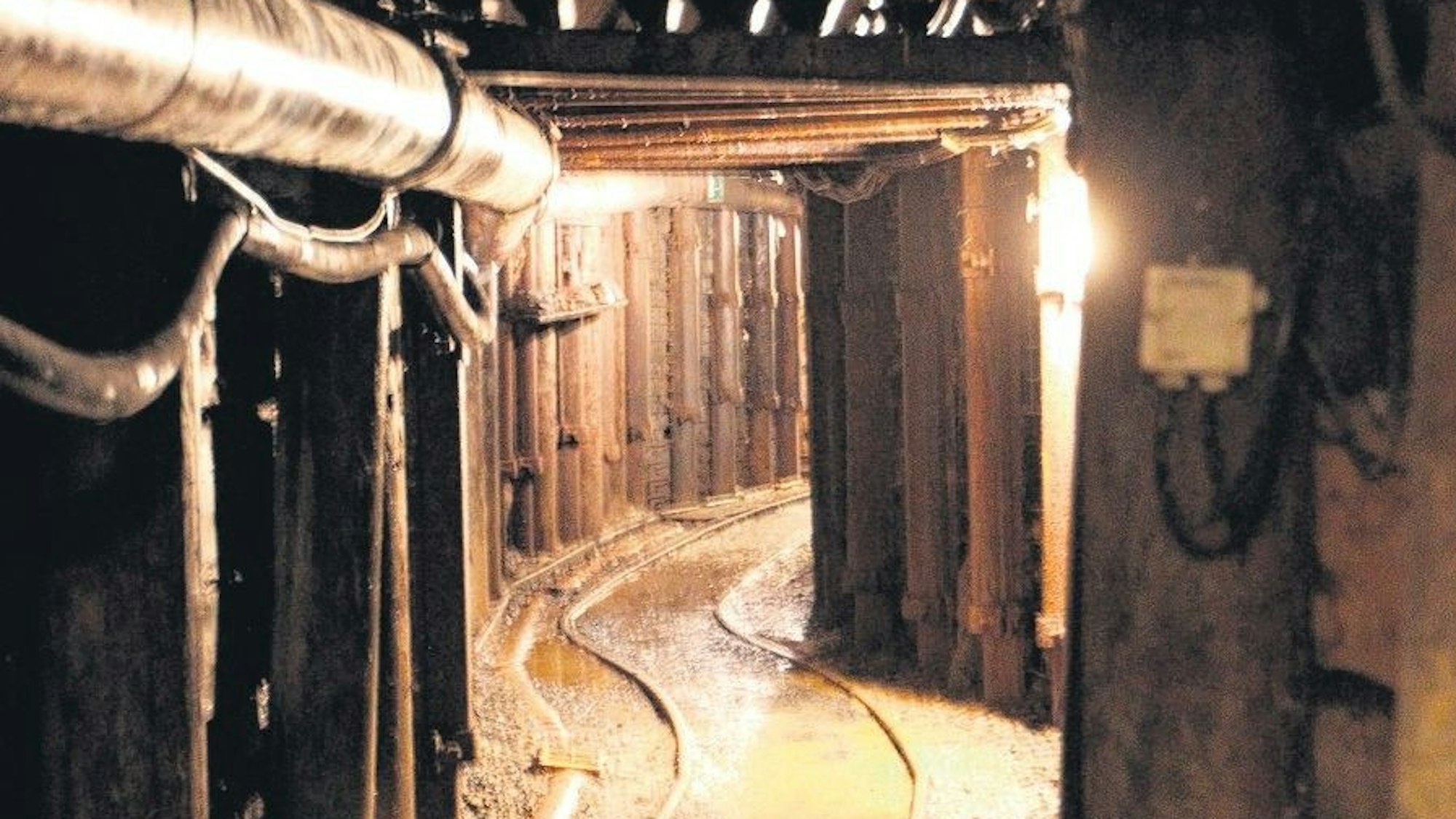 Blick in einen alten, engen Bergwerksstollen mit Schienen auf dem Boden.