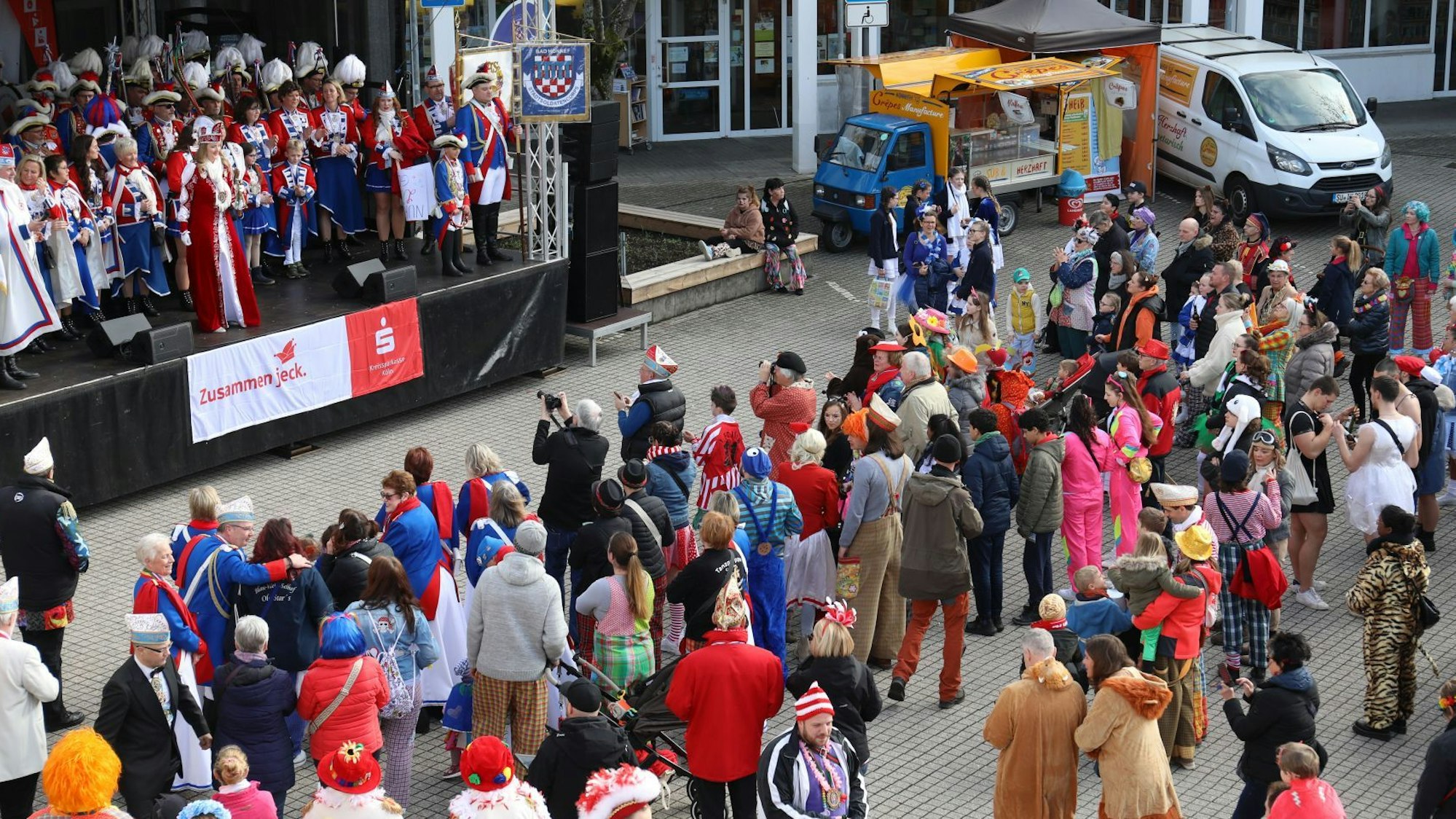 Viele kostümierte Jecken stehen vor einer Bühne.