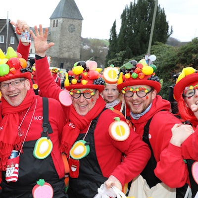 Menschen mit Obst auf den Hüten Stehen vor der Kürtener Kirche St. Johannes Baptist.