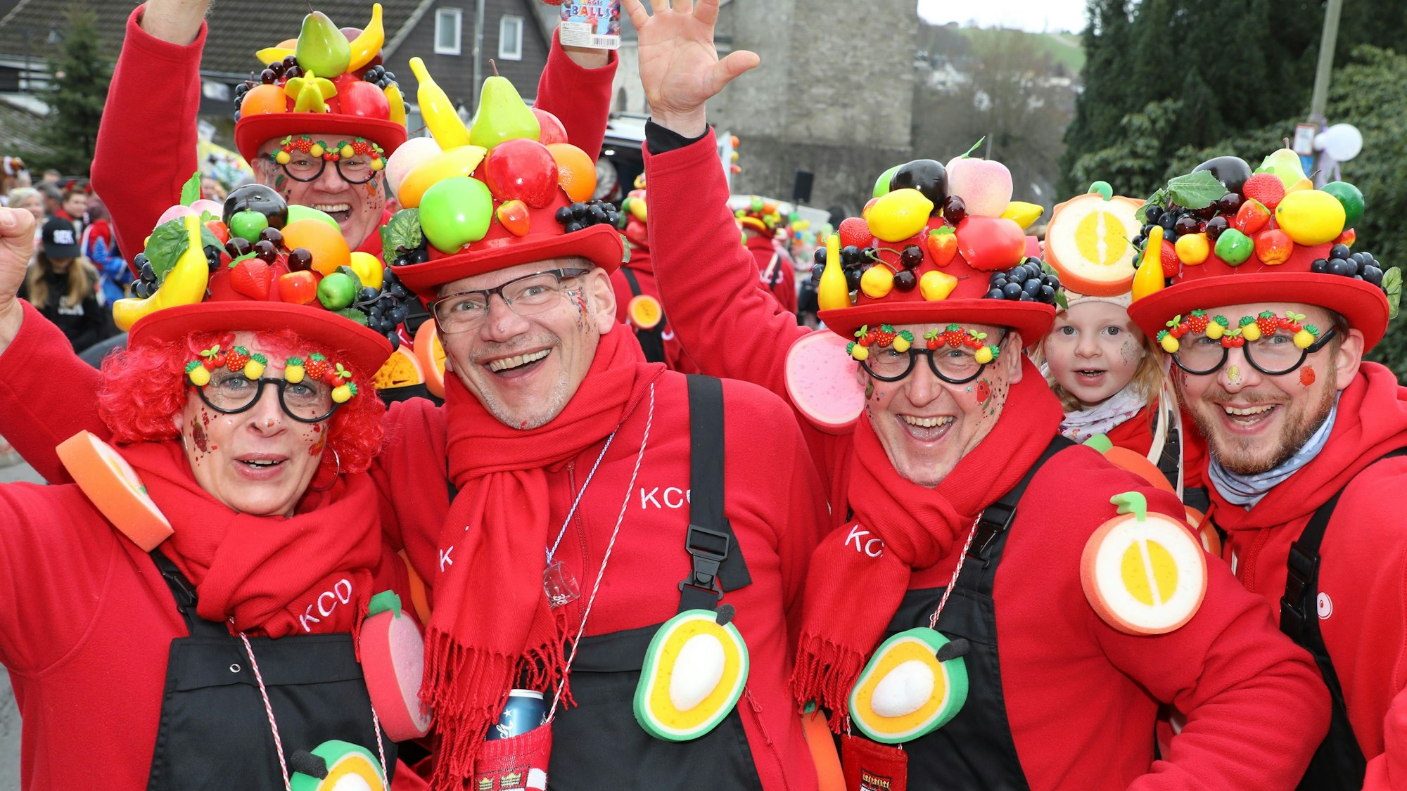 Menschen mit Obst auf den Hüten Stehen vor der Kürtener Kirche St. Johannes Baptist.