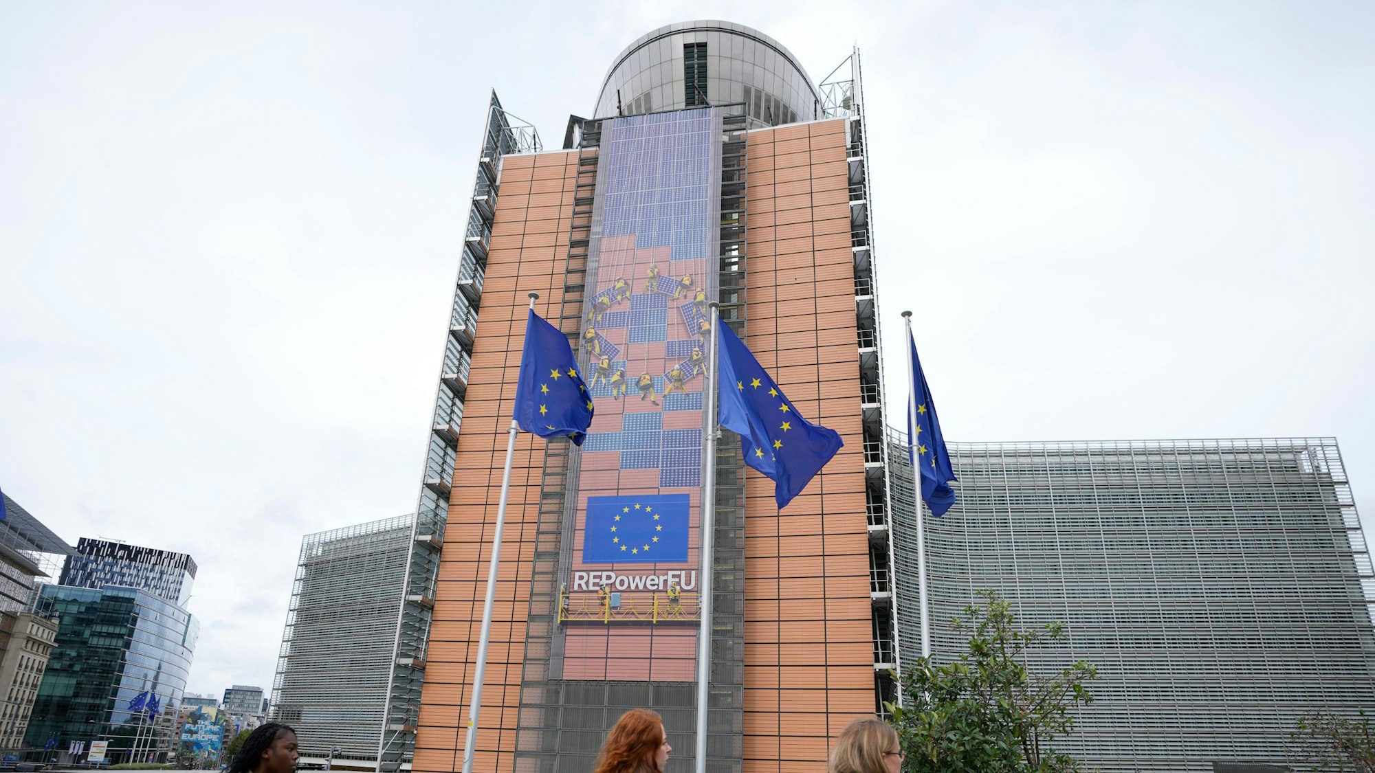 EU-Fahnen flattern im Wind, während Fußgänger am EU-Hauptsitz vorbeigehen.