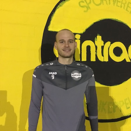 Fußballer Jannes Hoffmann steht vor einer gelben Wand mit dem Schriftzug „Eintracht“.