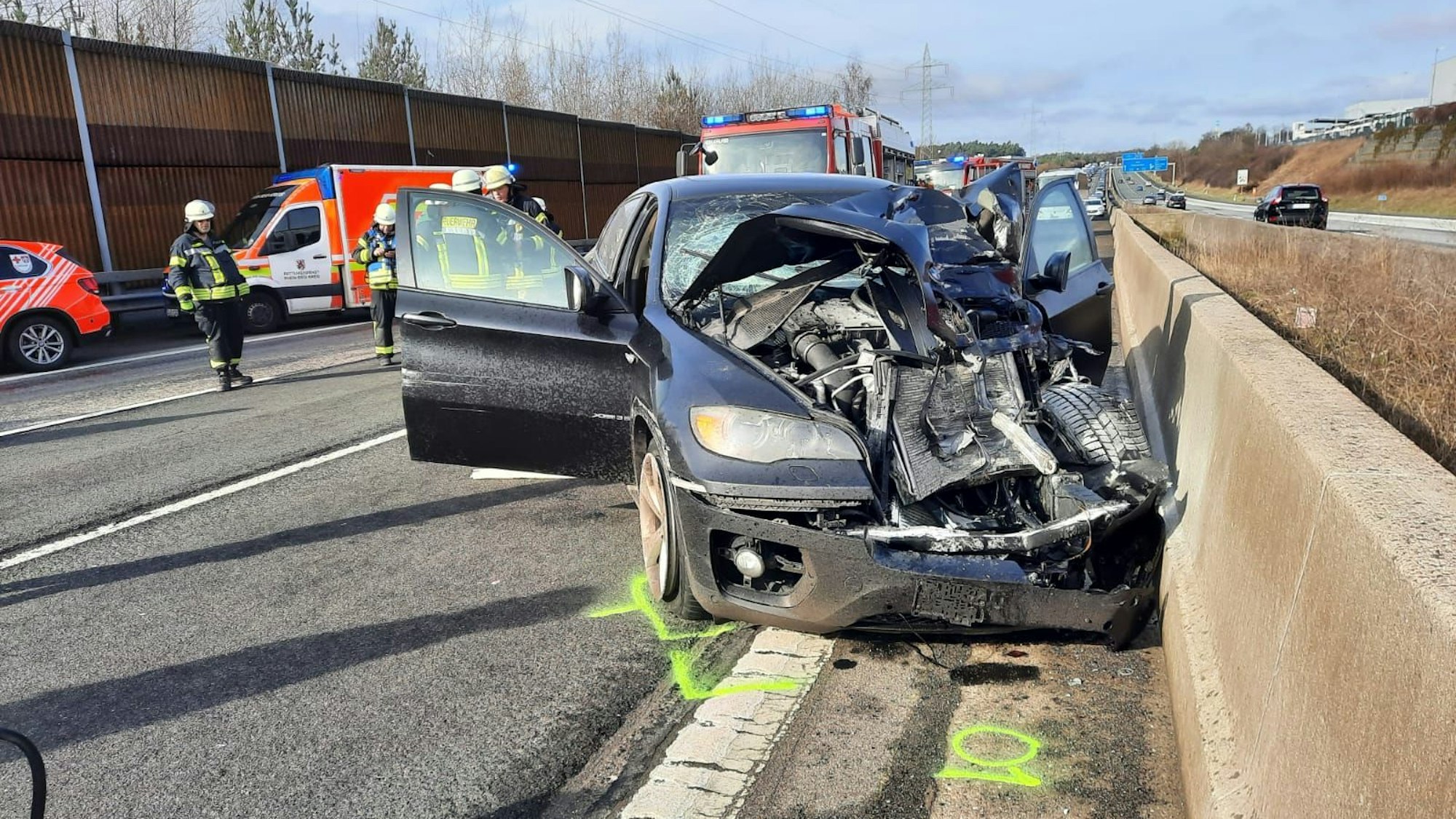 Ein blauer BMW mit stark verformter Front, im Hintergrund wartet ein Rettungswagen.