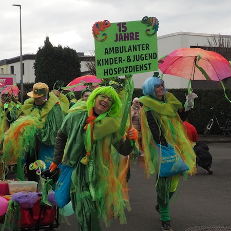 Menschen in bunten Kostümen sind mit einem Handwagen unterwegs.