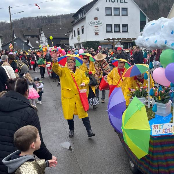 Eine mit Regenjacken und Schirmen auf dem Kopf verkleidete Gruppe, verteilt beim Karnevalszug in Gummersbach-Rebbelroth Kamelle.