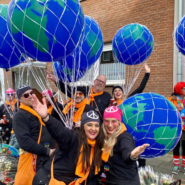 Eine Gruppe von Männern und Frauen mit orangefarbenen Schals, großen Ballons und Kopftüchern mit dem Friedenszeichen.