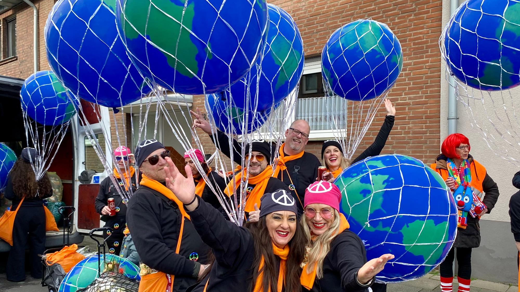 Eine Gruppe von Männern und Frauen mit orangefarbenen Schals, großen Ballons und Kopftüchern mit dem Friedenszeichen.