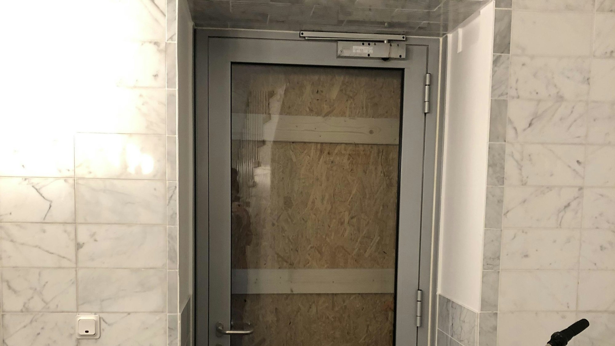 Eine Glastür, die von außen mit einer Spanplatte verbarrikadiert ist.
