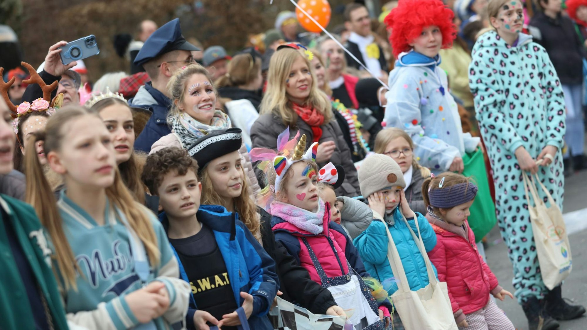 Bunt verkleidete Erwachsene und Kinder stehen an der Straße und haben Taschen dabei.