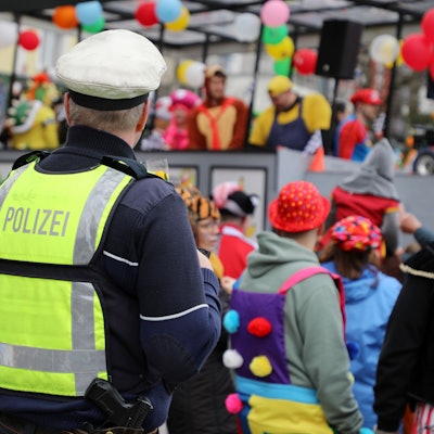 Ein Polizist steht an einem Karnevalszug und beobachtet das jecke Treiben.