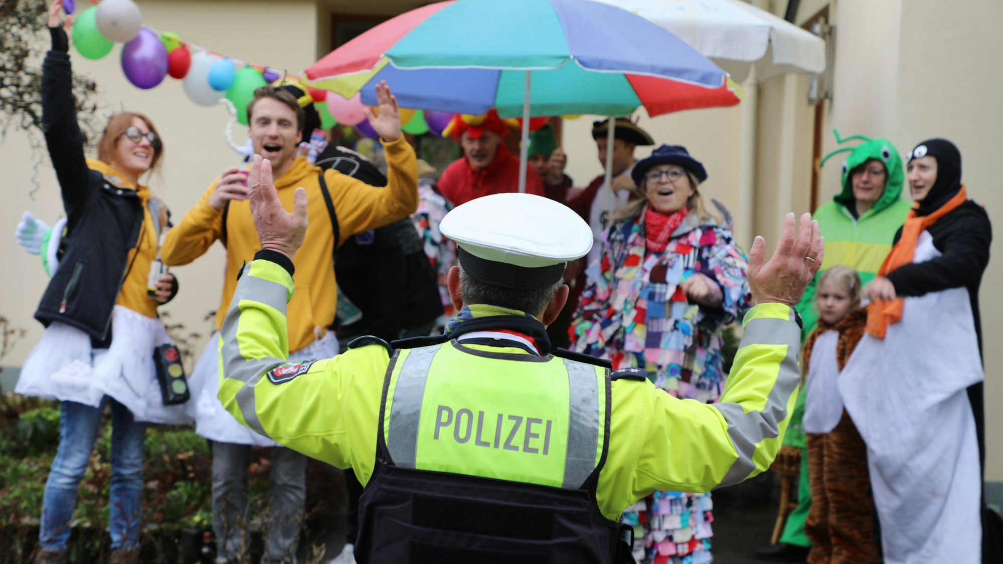 Ein Polizist steht am Rand des Karnevalszugs durch Bergisch Gladbach-Sand und winkt.