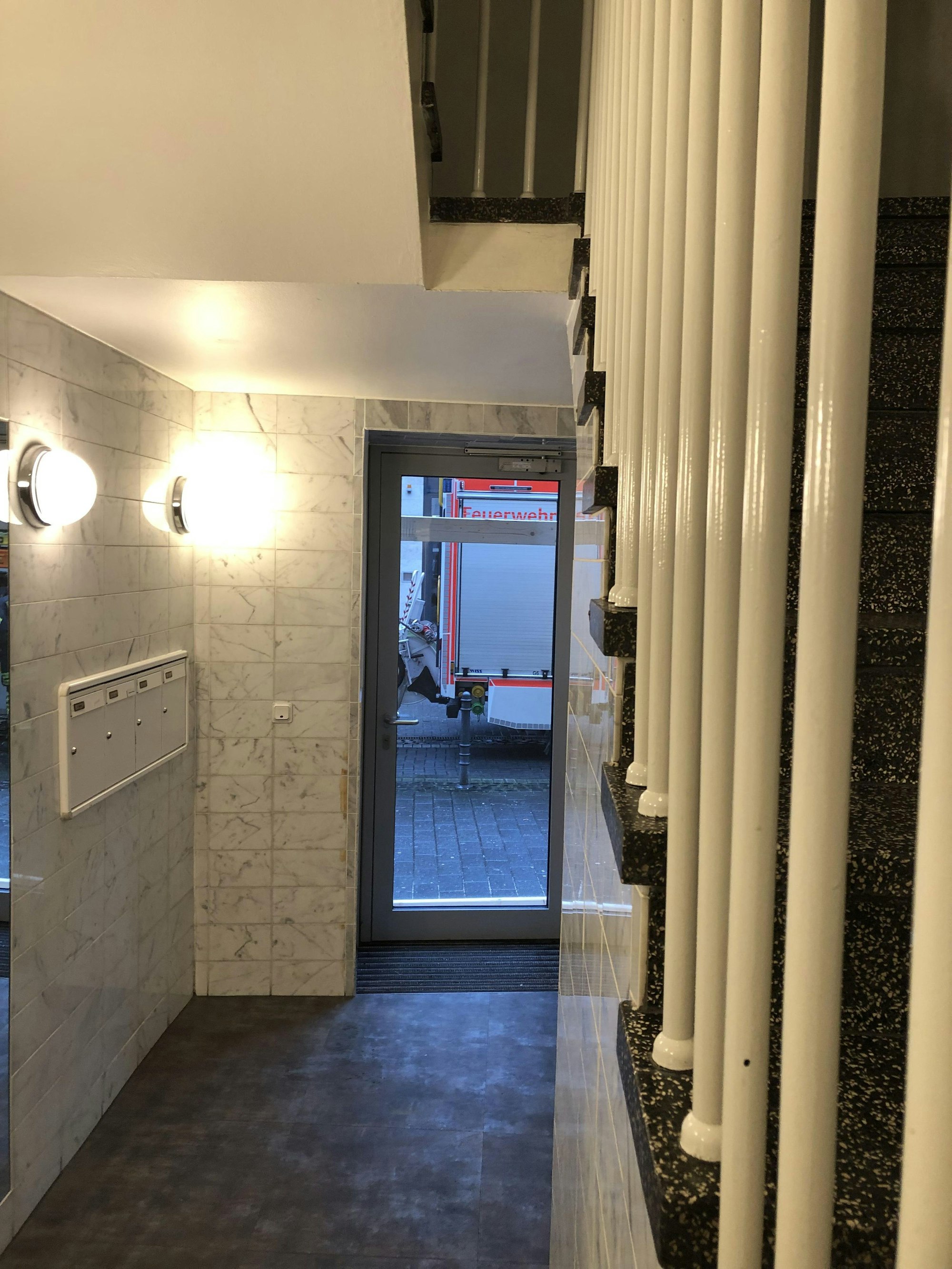 Ein Feuerwehrwagen ist aus einem Hausflur durch eine Glastür zu sehen.