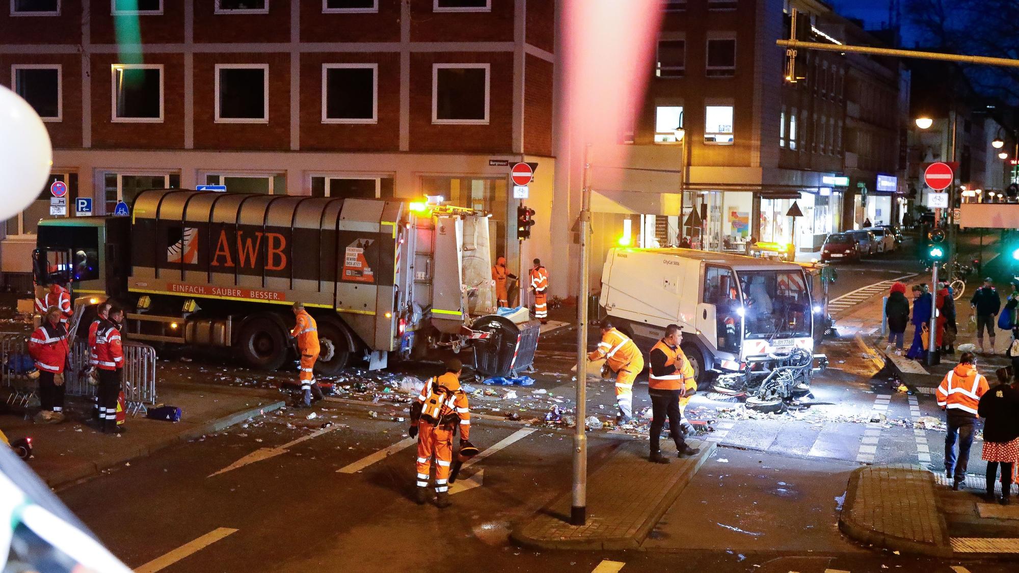 Die Mitarbeitenden der AWB folgen dem Rosenmontagszug und bringen die Straßen und Wege wieder in Ordnung. Hier sind zahlreiche Menschen dabei beschäftigt, die Kreuzung Burgmauer/Zeughausstraße zu säubern.