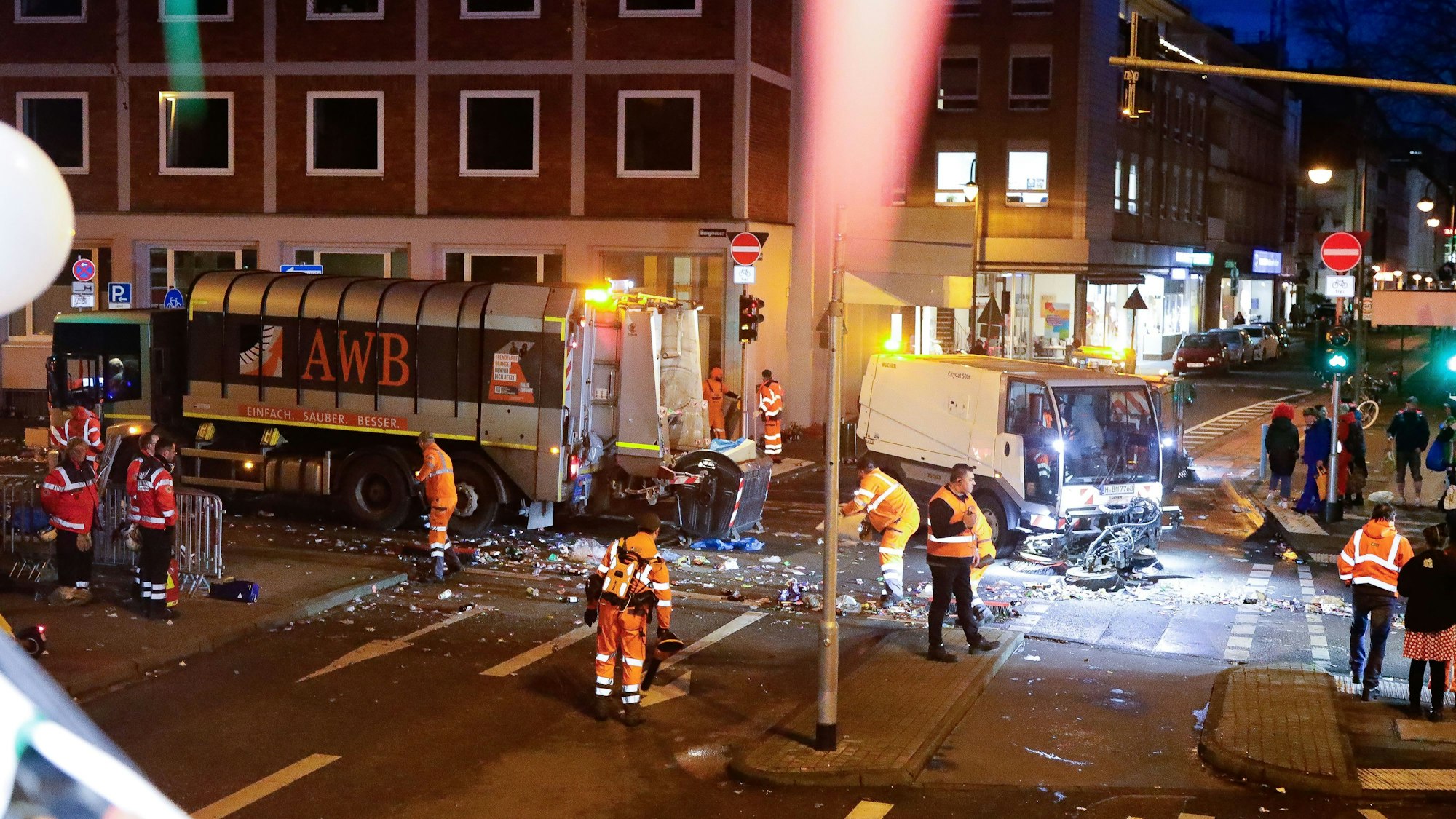 Die Mitarbeitenden der AWB folgen dem Rosenmontagszug und bringen die Straßen und Wege wieder in Ordnung. Hier sind zahlreiche Menschen dabei beschäftigt, die Kreuzung Burgmauer/Zeughausstraße zu säubern.