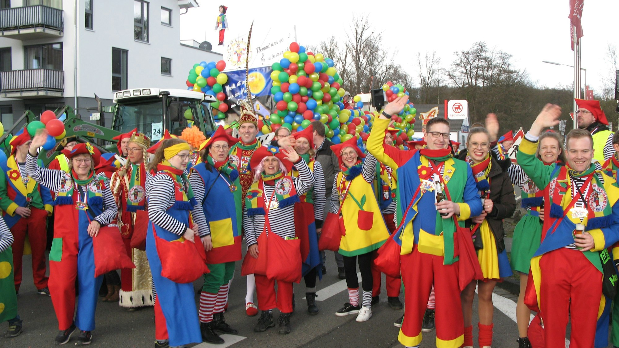 Männer und Frauen in leuchtend-bunten Anzügen stehen mit dem Dreigestirn vor einem Wagen, der mit bunten Luftballons geschmückt ist.