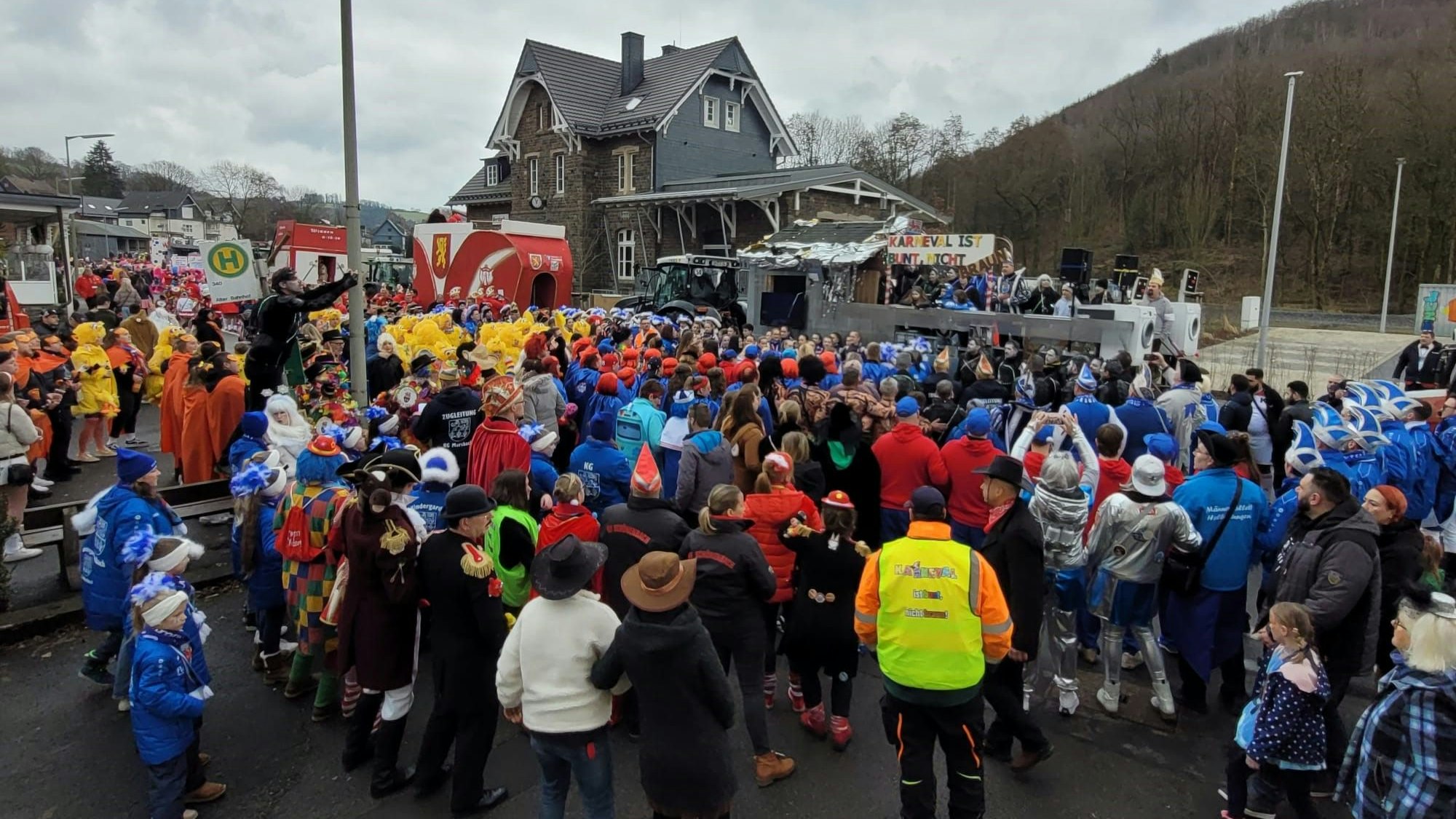 Zahlreiche Menschen stehen vor dem Prinzenwagen in Morsbach beisammen. Auf diesem ist ein Schild zu sehen, auf dem steht: „Karneval ist bunt, nicht braun“.