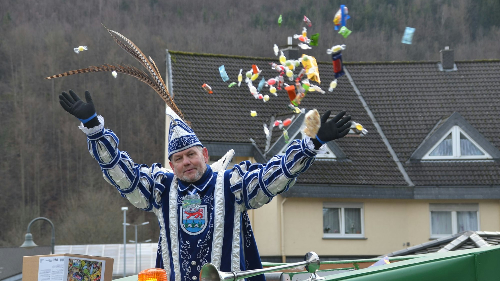 Ein Karnevalsprinz wirft Kamelle von einem Wagen.