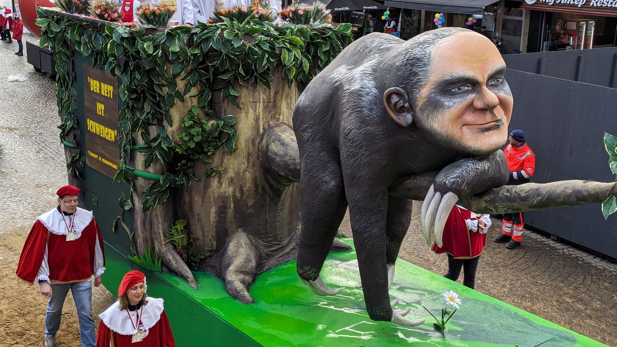Auf einem Mottowagen des Kölner Rosenmontagszugs wird Kanzler Olaf Scholz als Faultier dargestellt, das untätig auf einem Ast liegt. Der Kopf des Faultiers trägt die Gesichtszüge des Kanzlers.