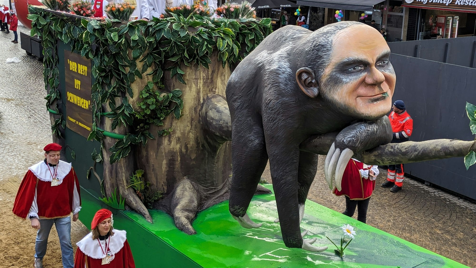 Auf einem Mottowagen des Kölner Rosenmontagszugs wird Kanzler Olaf Scholz als Faultier dargestellt, das untätig auf einem Ast liegt. Der Kopf des Faultiers trägt die Gesichtszüge des Kanzlers.