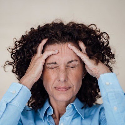 Frau hält sich die Hände an den Kopf und kneift die Augen zu.