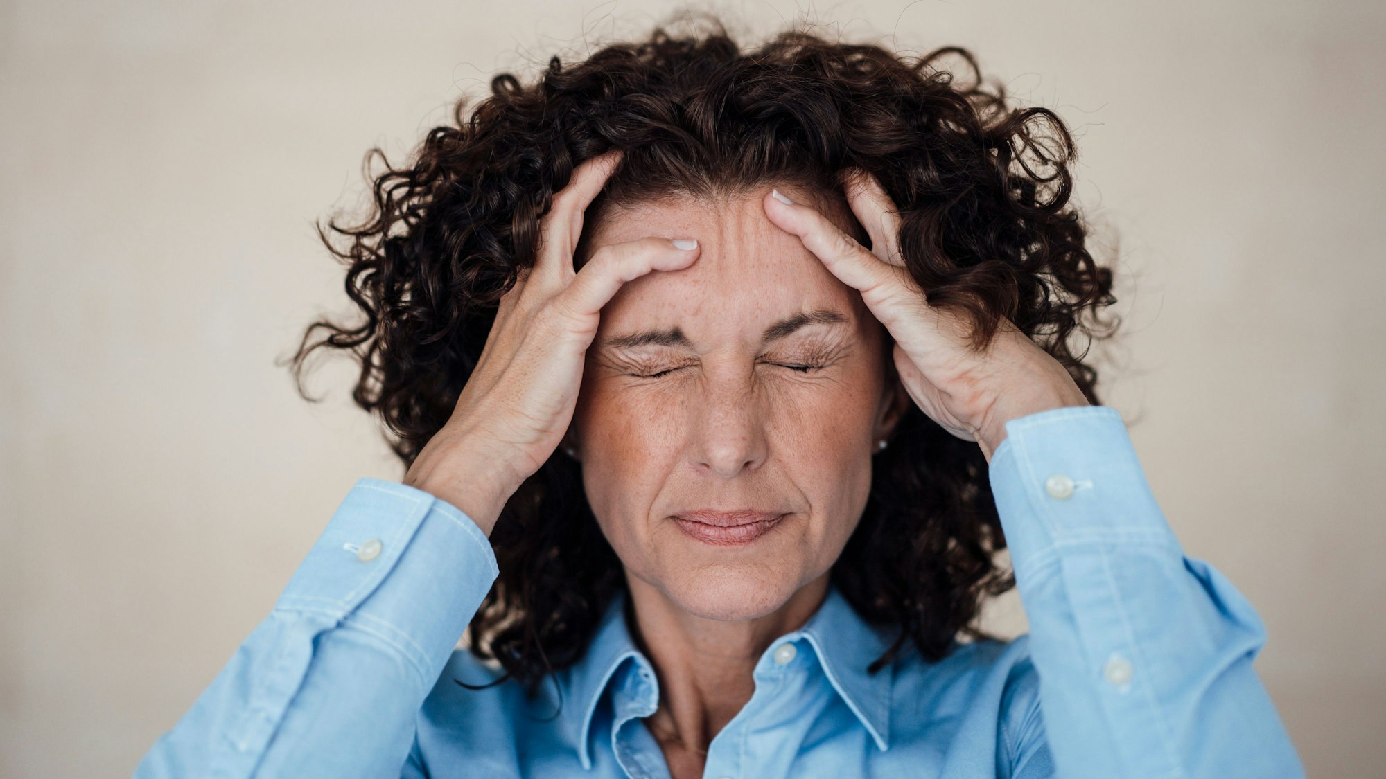 Frau hält sich die Hände an den Kopf und kneift die Augen zu.