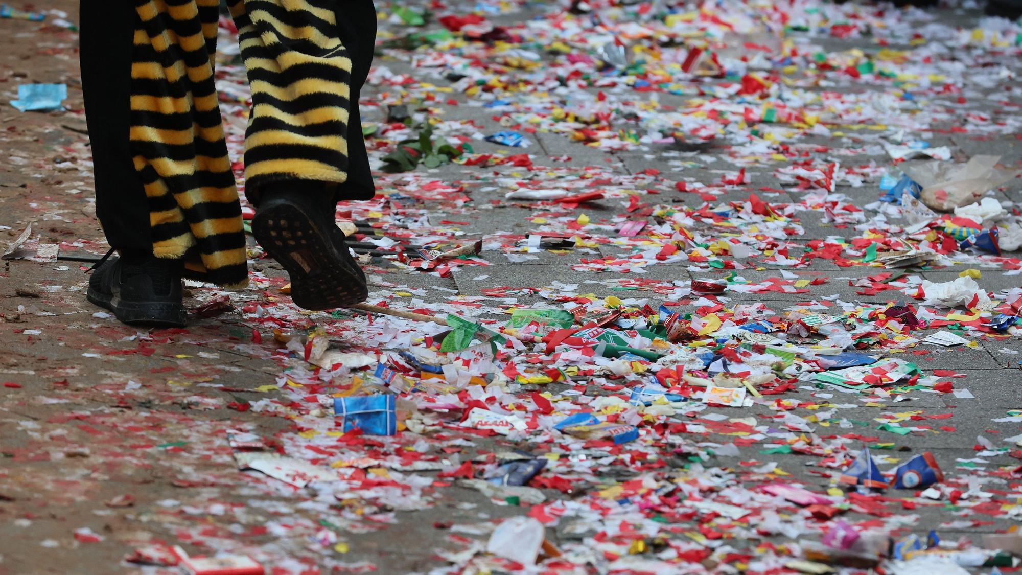 Müll vom Rosenmontagszug auf der Straße, Hose und Schuhe einer kostümierten Person sind zu sehen.