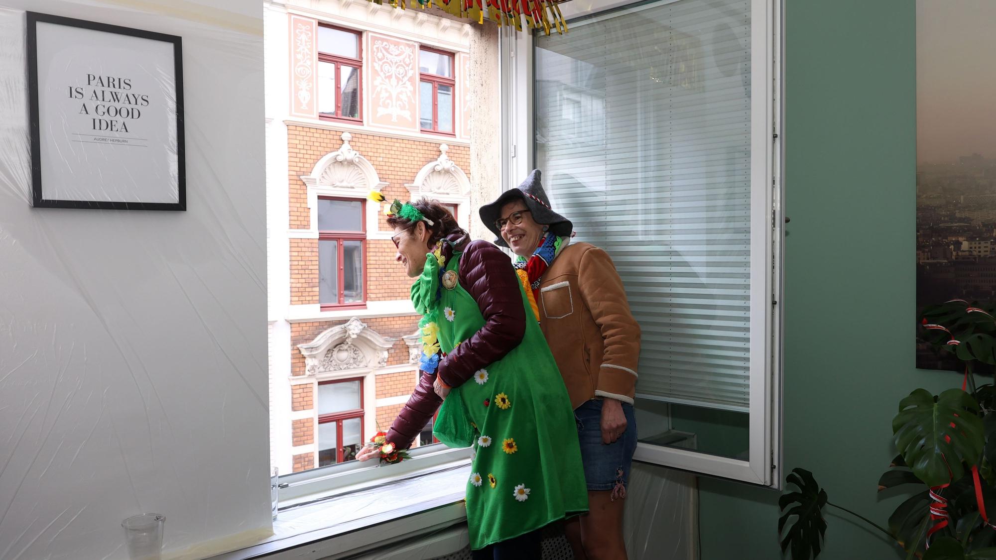 Die Französinnen Beatrice und Christine schauen den Rosenmontagszug aus dem Wohnzimmerfenster. Der Frankreich-Bezug der Familie ist in der Wohnung überall zu sehen.