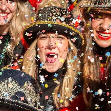 Drei verkleidete Frauen in buntem Konfettiregen.