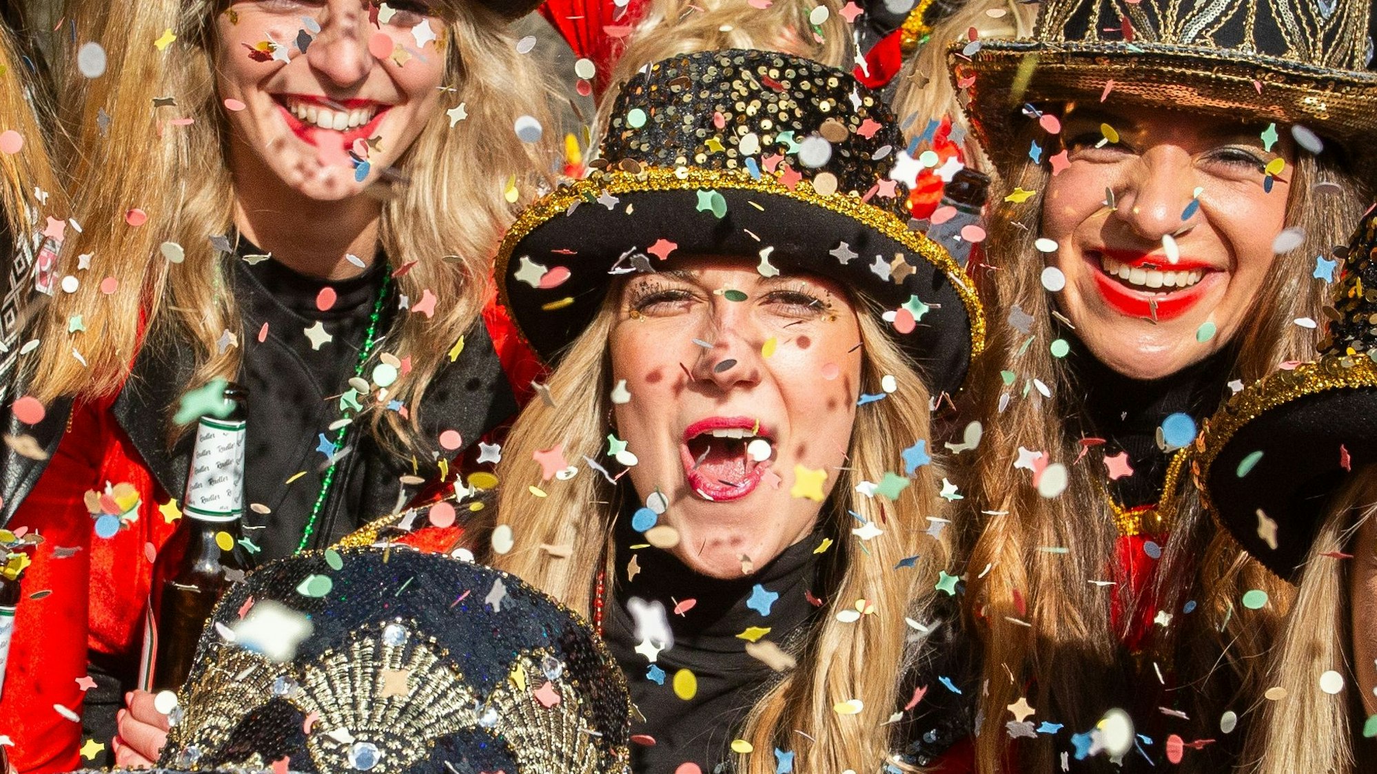 Drei verkleidete Frauen in buntem Konfettiregen.