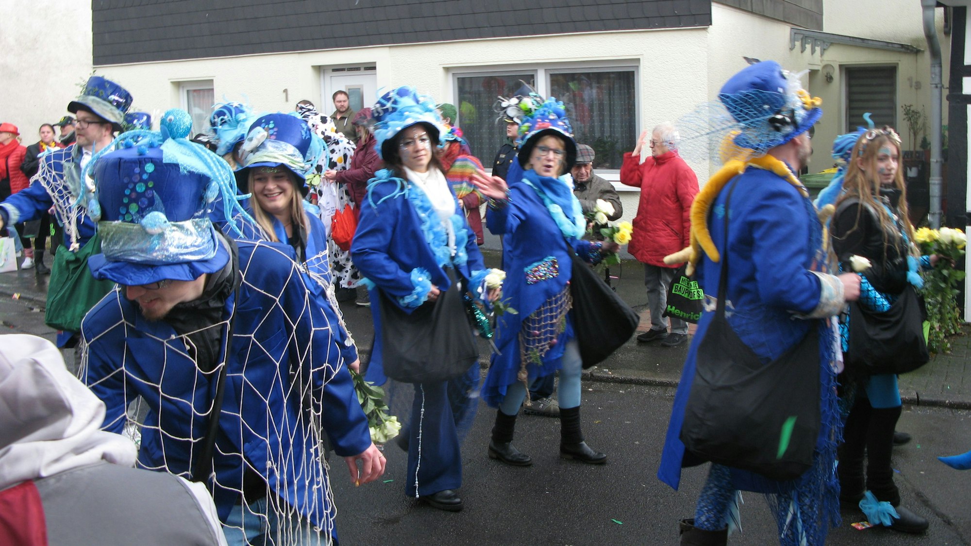 Männer und Frauen gehen tiefblauen Fracks und mit ebenso blauen Hüten im Zug mit.