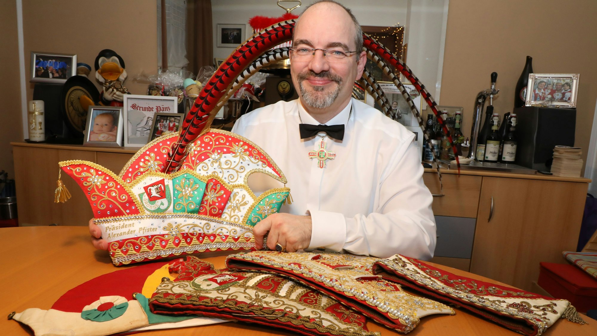 Der Präsident der Großen Gladbacher KG, Alexander Pfister, sitzt an einem Tisch mit seiner neuen Präsidentenkappe zum elfjährigen Amtsjubiläum. Auf dem Tisch: weitere Kappen teils aus den 20er Jahren (l.) und von seinem Vor-Vorgänger Franz Heinrich Krey