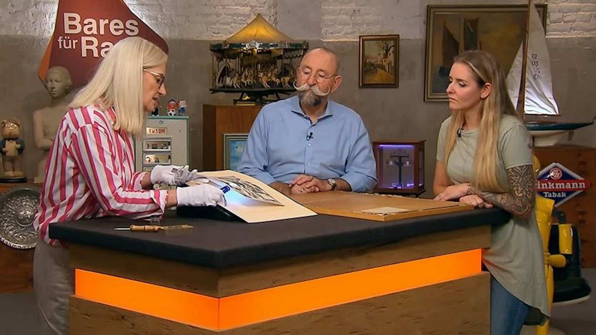Expertin Dr. Friederike Werner (l.) begutachtet den Dürer-Holzschnitt bei Bares für Rares. Ihrer Expertise lauschen ZDF-Moderator Horst Lichter (M.) und Verkäuferin Sarah Nickel (r.) aus Köln.