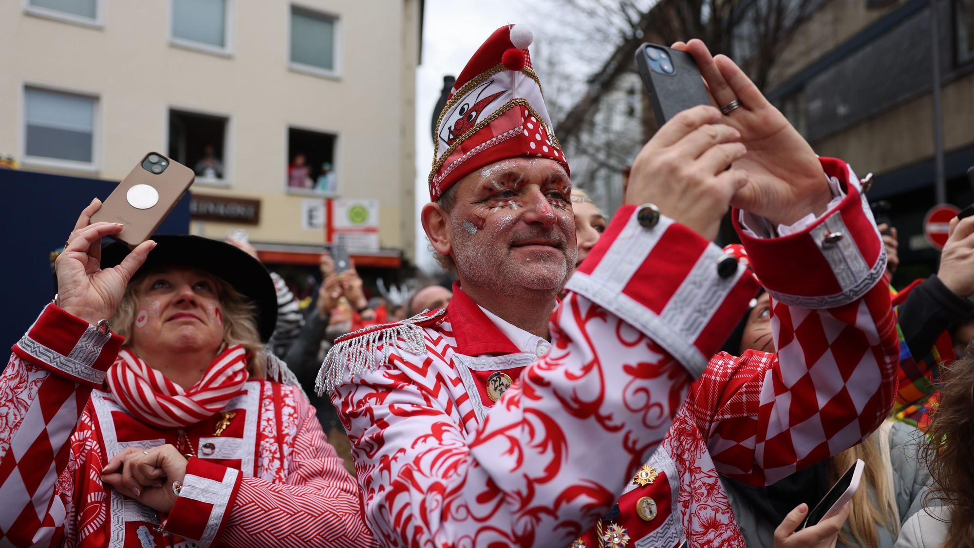 Jecken mit ihren Handys stehen am Rand des Rosenmontagsumzugs.