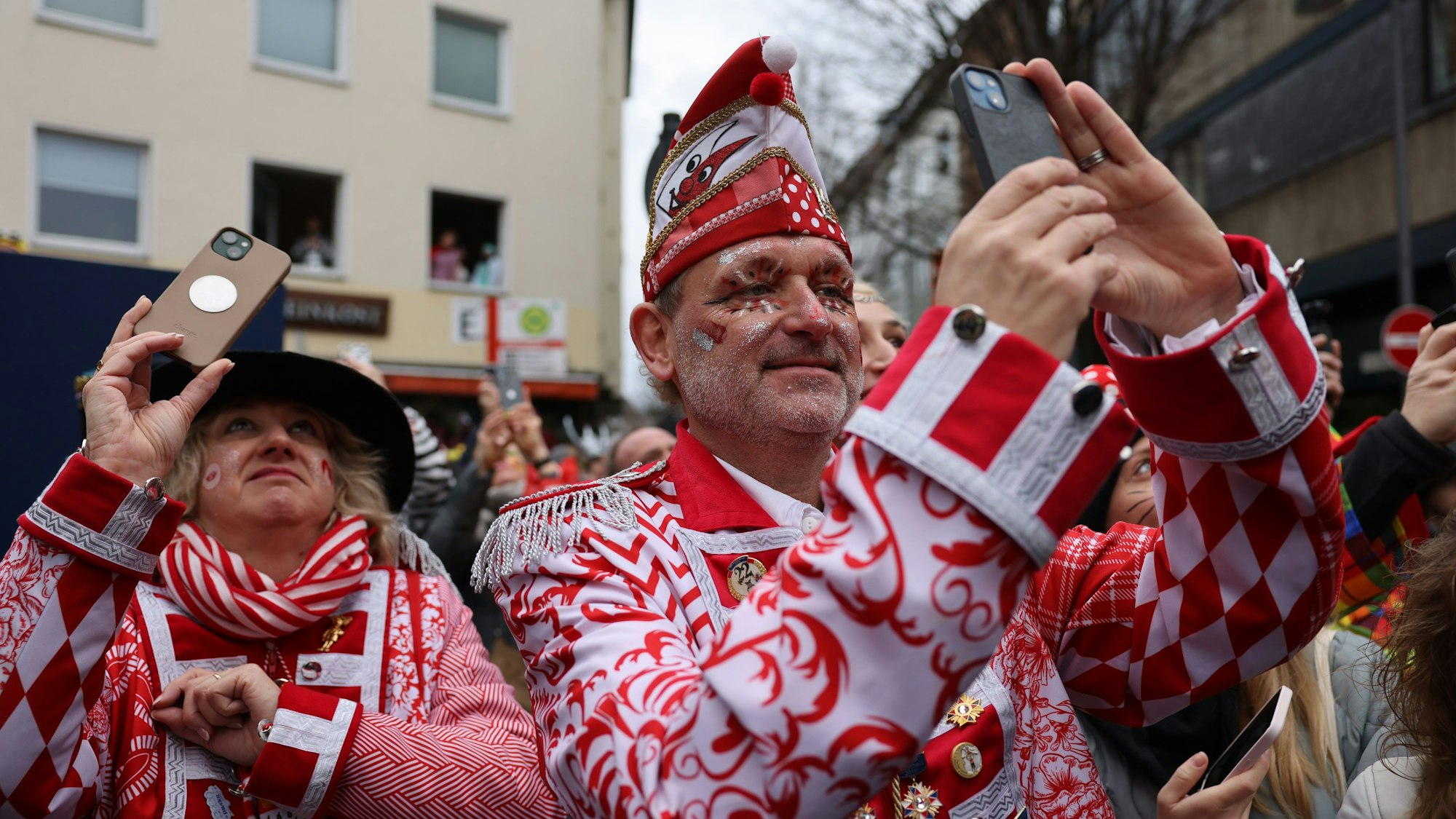 Jecken mit ihren Handys stehen am Rand des Rosenmontagsumzugs.