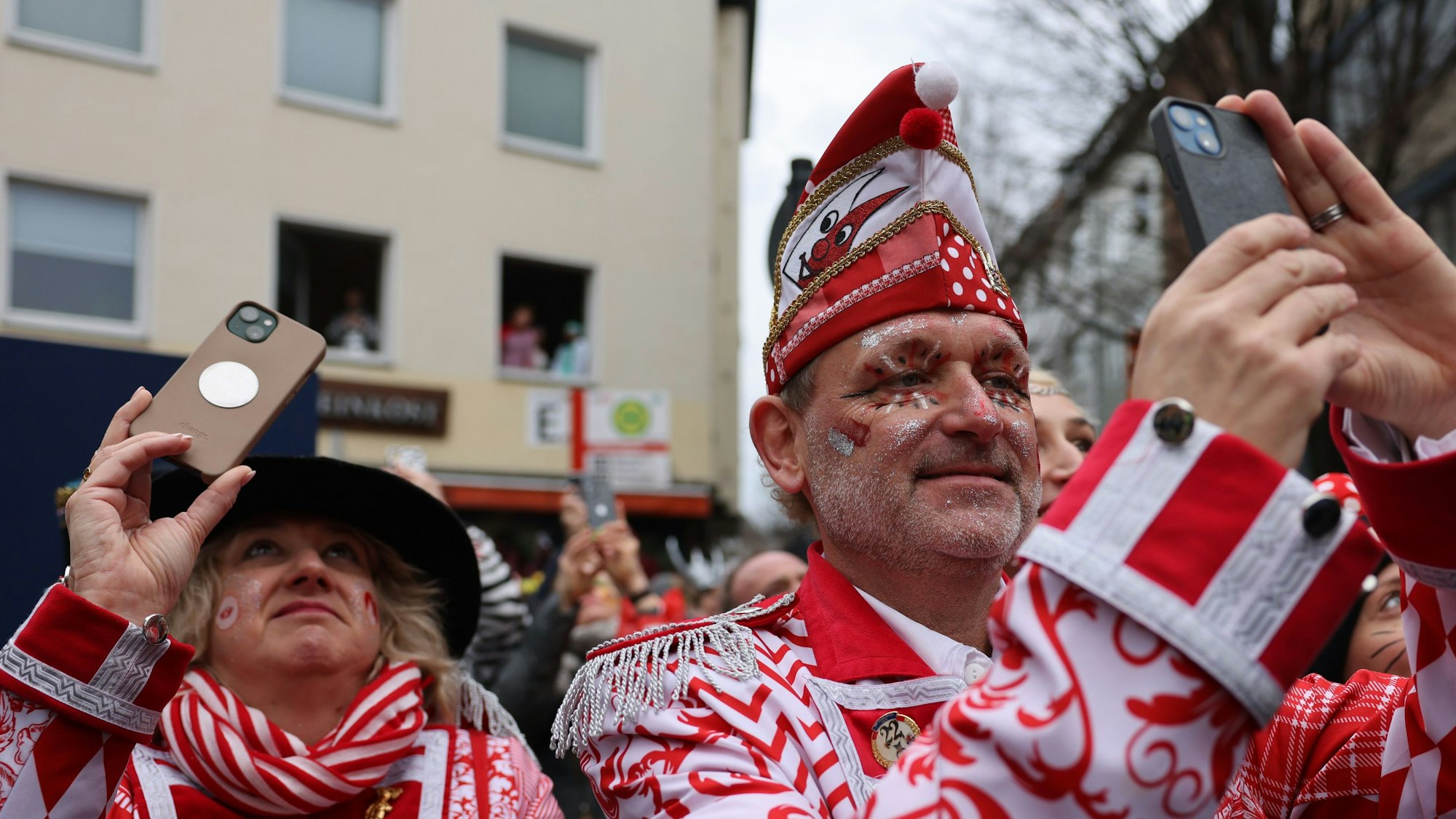Jecken mit ihren Handys stehen am Rand des Rosenmontagsumzugs.