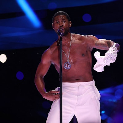 Usher auf der Bühne im Allegiant-Stadion während der Halbzeit-Show des 58. Super Bowls. Er singt ins Standmikrofon, zieht dabei sein weißes T-Shirt aus.