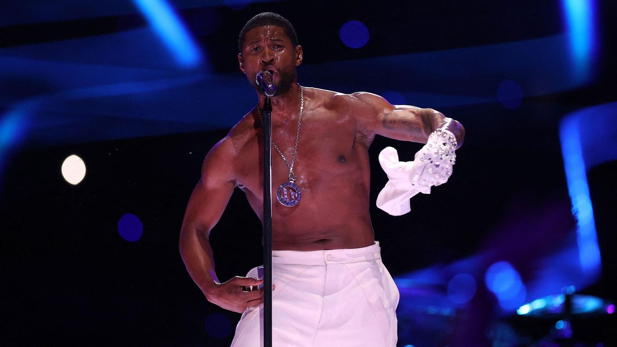 Usher auf der Bühne im Allegiant-Stadion während der Halbzeit-Show des 58. Super Bowls. Er singt ins Standmikrofon, zieht dabei sein weißes T-Shirt aus.