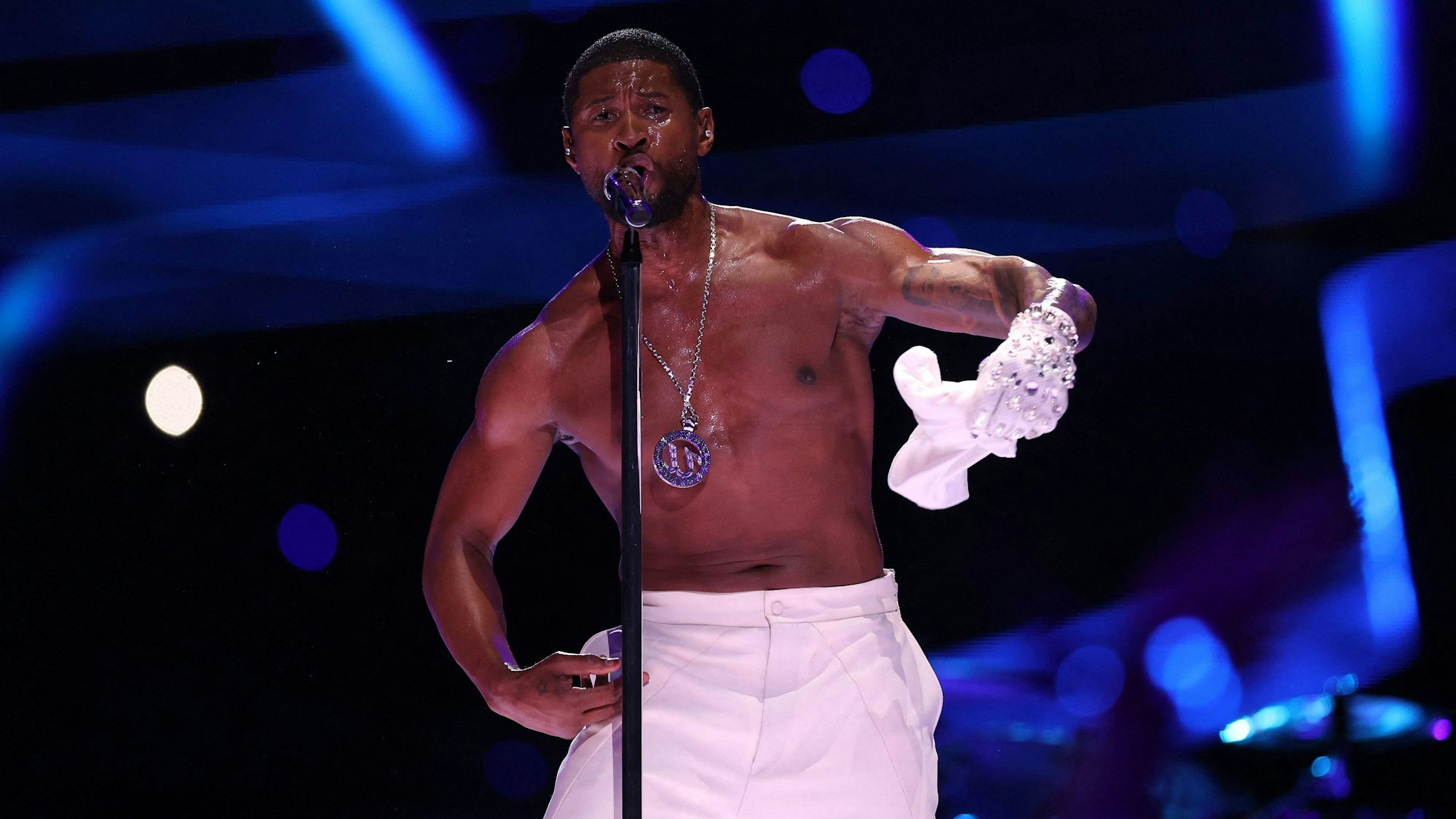 Usher auf der Bühne im Allegiant-Stadion während der Halbzeit-Show des 58. Super Bowls. Er singt ins Standmikrofon, zieht dabei sein weißes T-Shirt aus.