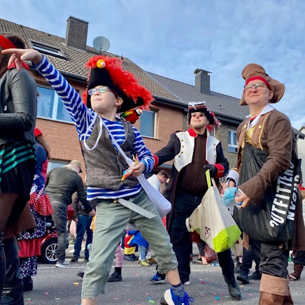 Zu sehen sind kostümierte Menschen, die beim Karnevalszug Süßigkeiten werfen.