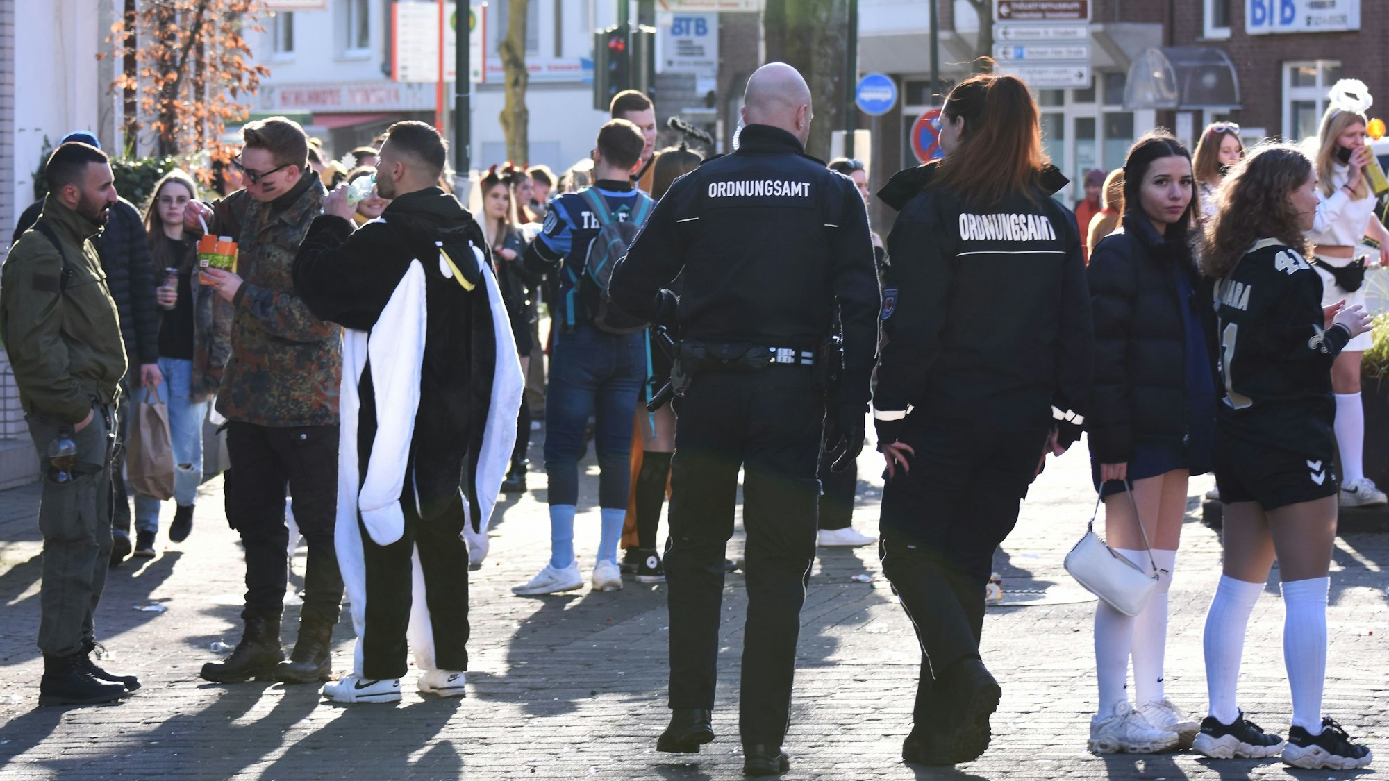 Mitarbeitende des Ordnungsamts laufen an Weiberfastnacht in Schlebusch durch die Menge der Kostümierten.